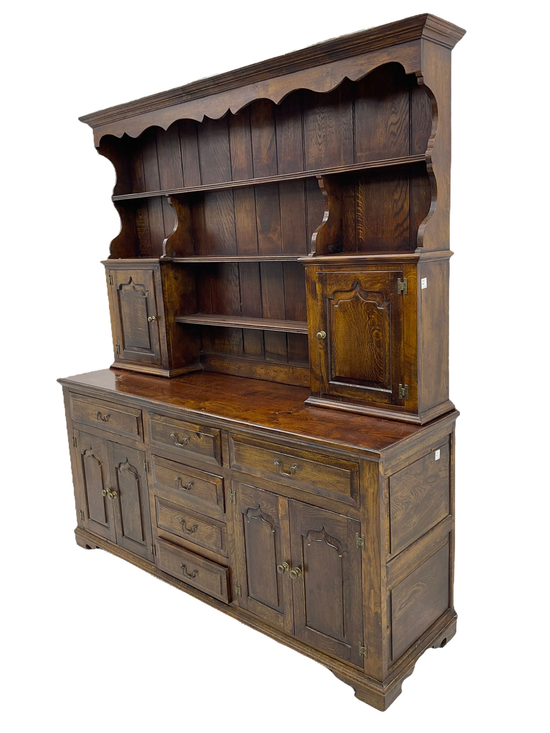 Traditional oak dresser, the moulded cornice over shaped apron, three heights plate rack fitted with two cupboards, the base fitted with six drawers and two double cupboards, panelled pointed ogee arched doors, on bracket feet