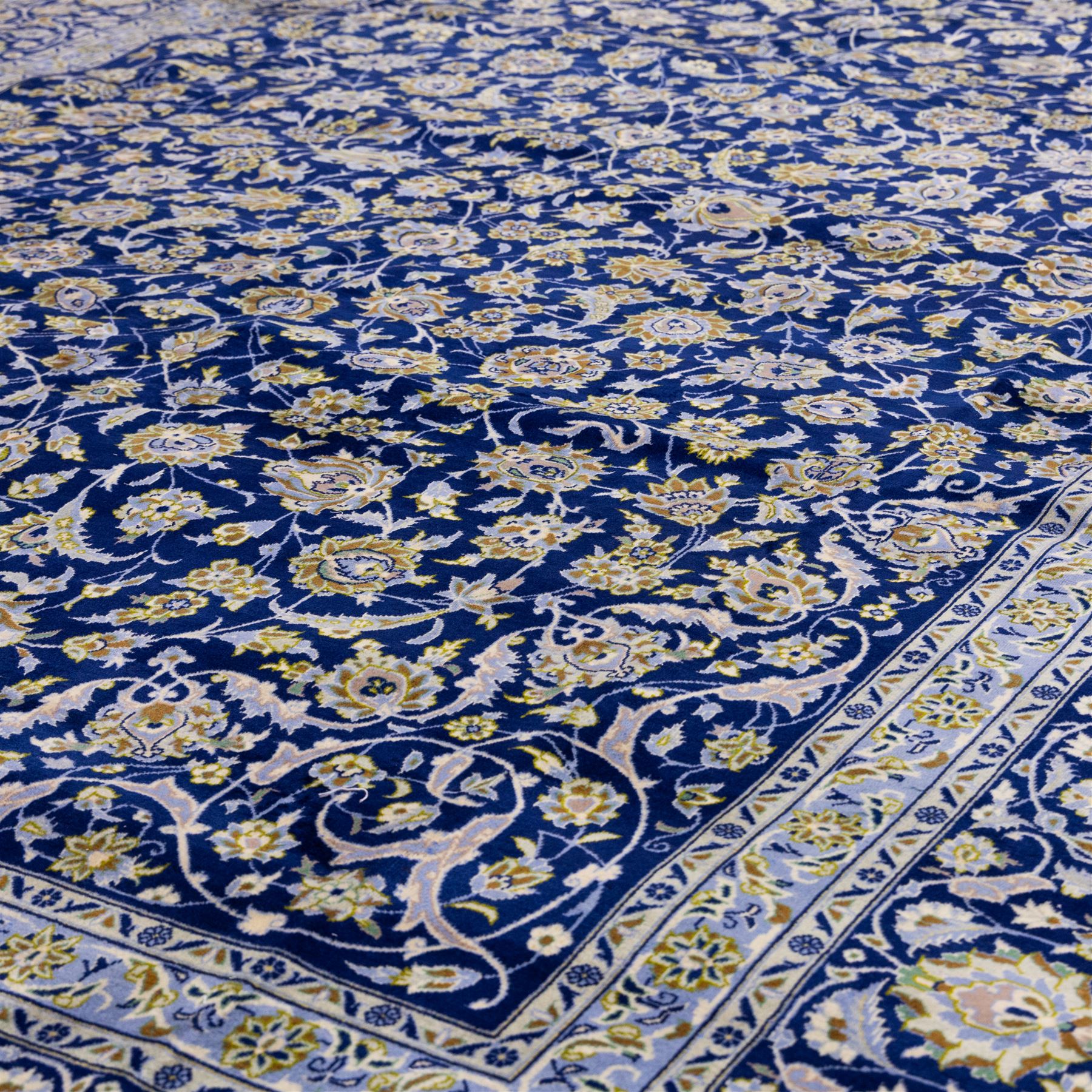 Central Persian Kashan hand-knotted carpet, deep indigo blue field densely decorated with all-over vine, palmette and flowering sprays arranged in a symmetrical pattern enclosed by broad navy border of stylized palmettes, and foliate vine decoration between multiple guard stripes, with cotton fringe ends 