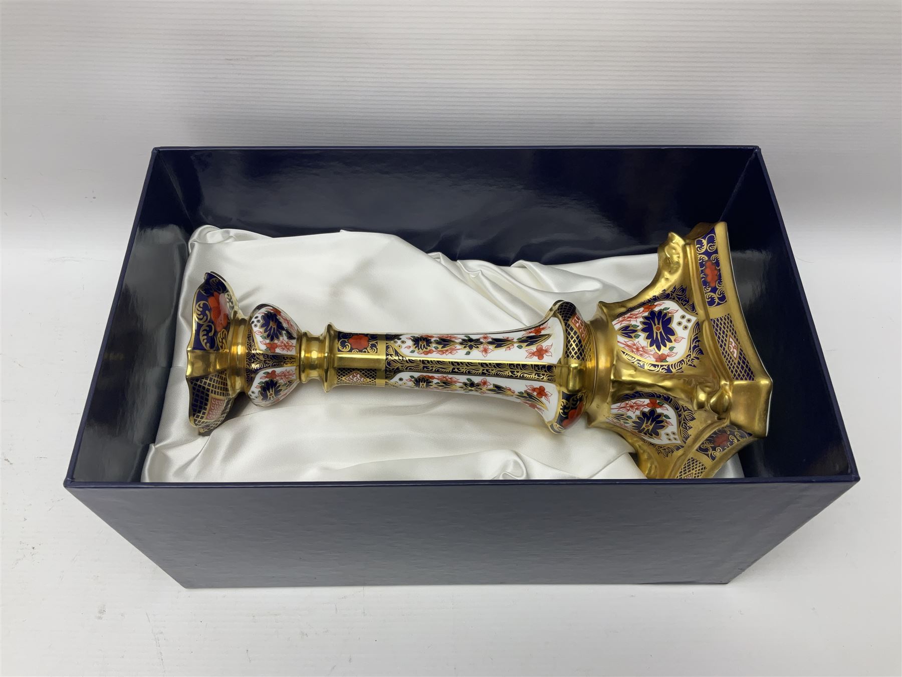 Pair of modern Royal Crown Derby Old Imari 1128 pattern candlesticks, each with shaped drip tray affixed to squat socket, upon spreading stem and canted square base with gilt dolphin edges, with printed marks beneath including Roman numeral year cypher for 2003, H26.5cm, with original boxes