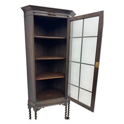 Early 20th century oak corner display cabinet, the moulded canted cornice over a single glazed door with geometric astragal bars, shelved interior, the lower tier forming a triangular platform, raised on four barley-twist supports united by shaped brackets