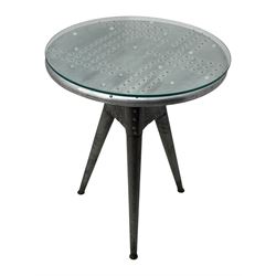 Contemporary industrial design riveted metal table, by repute fashioned from salvaged aeroplane parts, with a circular glass top on a tripod base, accompanied by three adjustable stools upholstered in burgundy