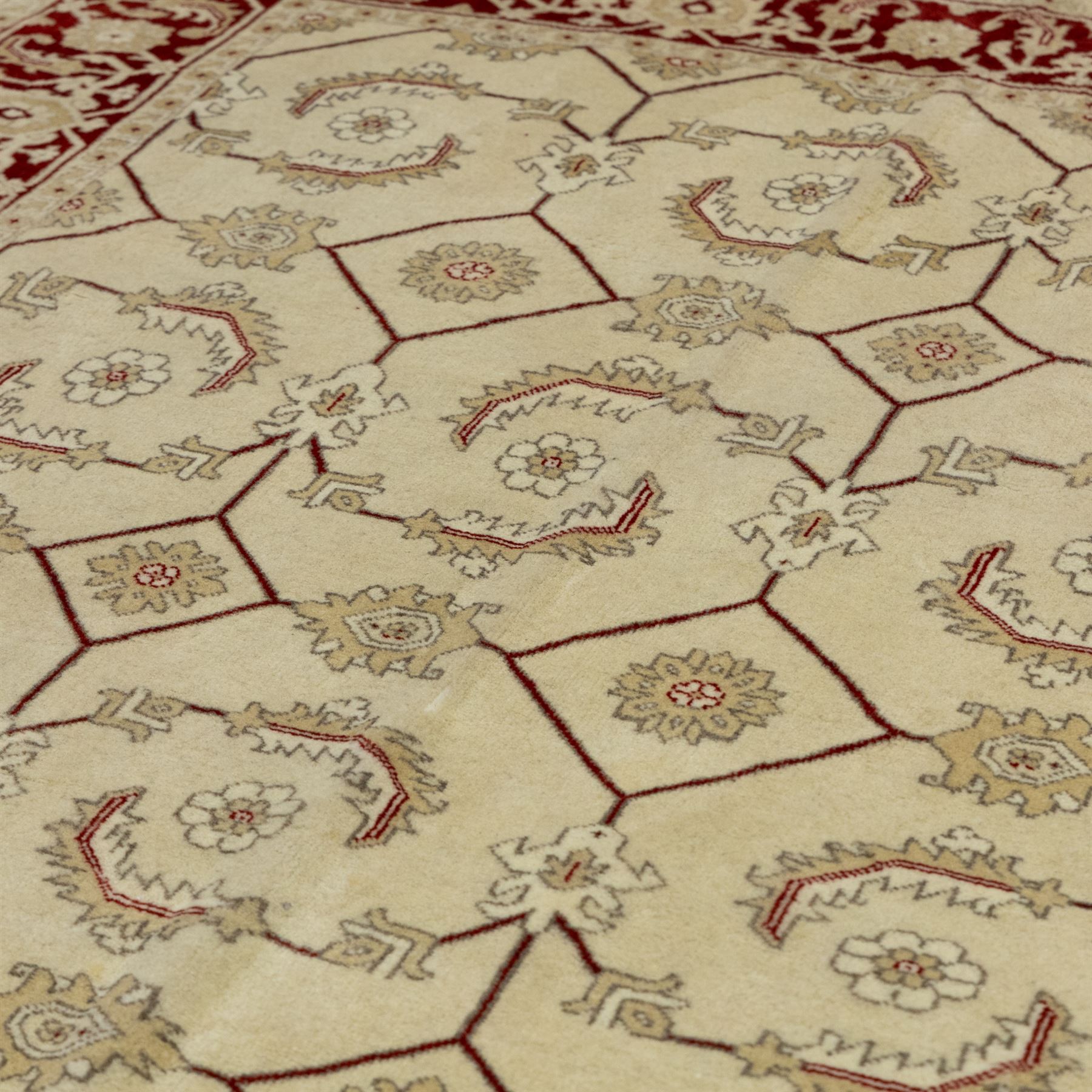 Baluchi signed hand-knotted rug, ivory ground, with an all-over geometric lattice design incorporating stylised flowerheads, hooked motifs and angular vine work, enclosed by a crimson border with repeating floral motifs and scrolling vines, flanked by narrow patterned guard stripes, signed to one corner, with cotton fringes