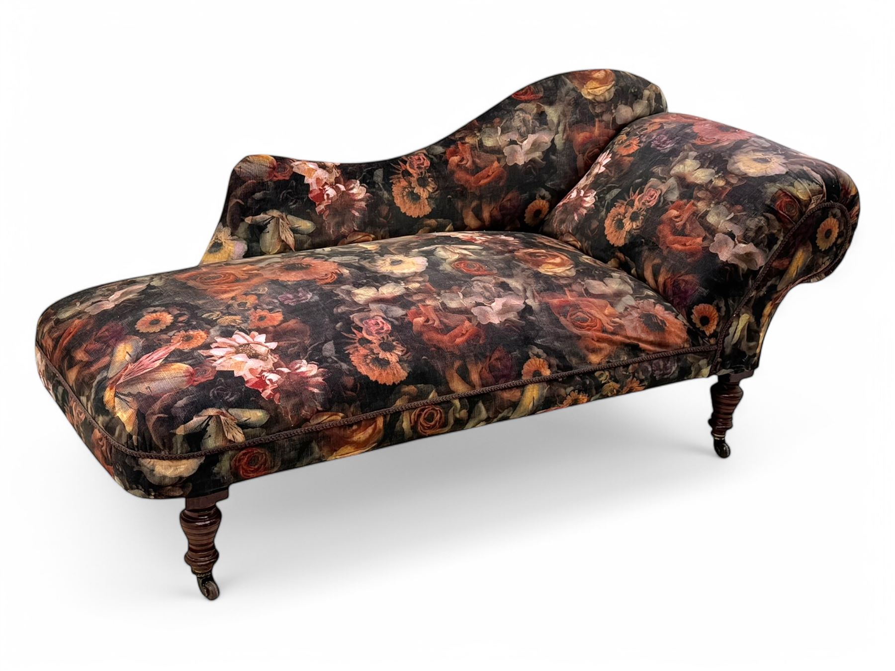 Victorian hardwood-framed chaise longue, serpentine back with rolled arm, upholstered in floral pattern fabric, on ring turned legs with ceramic castors 