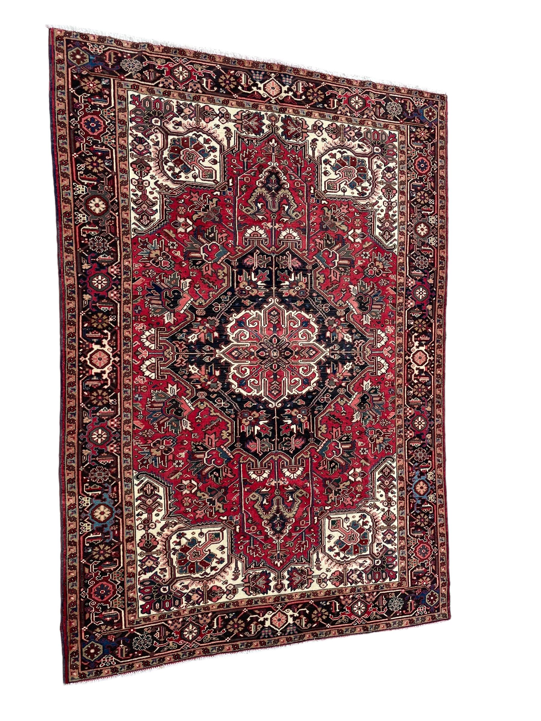 Persian Heriz red ground rug, central scrolled medallion on dark ground decorated with floral motifs, the surrounding field decorated with stylised plant motifs and smaller geometric symbols, guarded border with repeating pattern punctuated with rosettes and flower heads 