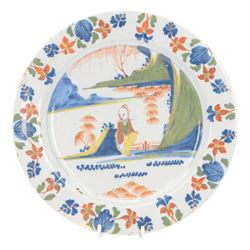 Mid 18th century Lambeth Delft plate, probably from the Abigail Griffith factory, circa 1750, painted in polychrome enamels with a figure seated in a landscape, within a garlanded border of flowers to rim, D34cm, together with a Liverpool Delft plate, circa 1760, painted in blue with a boathouse surrounded by trees by a river, within diaper and cell borders, D37cm
