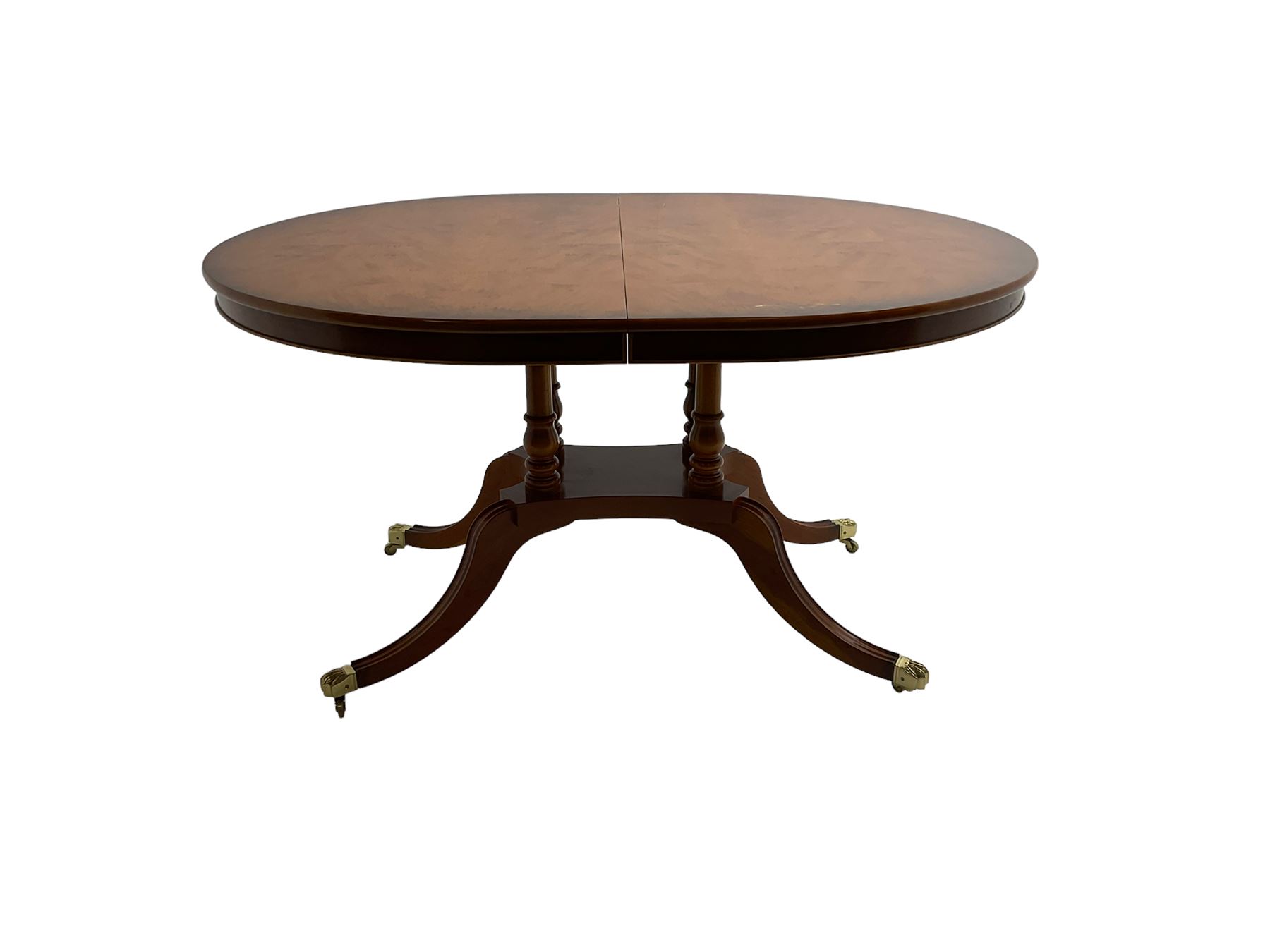 Georgian design yew wood twin pedestal dining table, circular top over four turned columns joined by base, raised on splayed and fluted cabriole supports with paw feet and castors (140cm x 108cm x 77cm); with set six (4+2) Georgian style yew wood dining chairs, middle rail pierced and carved with flowerhead and extending foliage, upholstered drop in seat, raised on turned tapering supports (50cm x 47cm x 86cm)