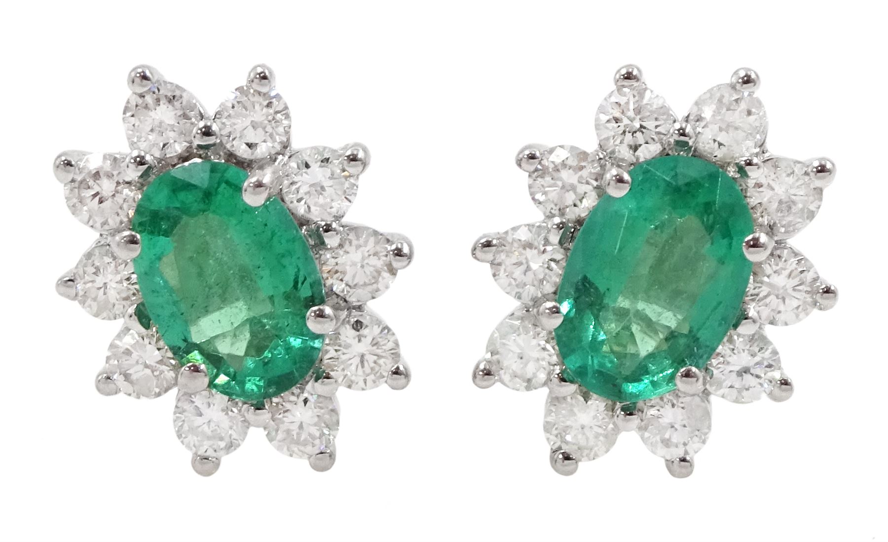 Pair of 18ct white gold emerald and diamond earrings, each stud set with a single oval cut emerald, surrounded by ten round brilliant cut diamonds, stamped, total emerald weight approx 0.90 carat, total diamond weight approx 0.55 carat