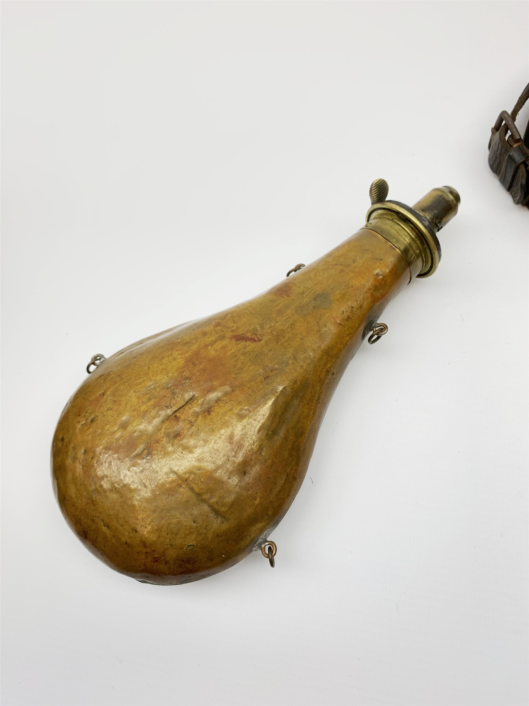 Victorian large copper powder flask embossed with a hunting scene within an oak leaf border with stag and fox heads, the nozzle marked 'Extra Quality Sykes Patent', fitted with four suspension rings H24cm; together with Victorian leather shoulder shot flask with Sykes nozzle L80cm (2)