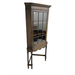 Early to mid-20th century oak corner display cabinet, projecting cornice over astragal glazed door, on spiral turned supports joined by stretchers