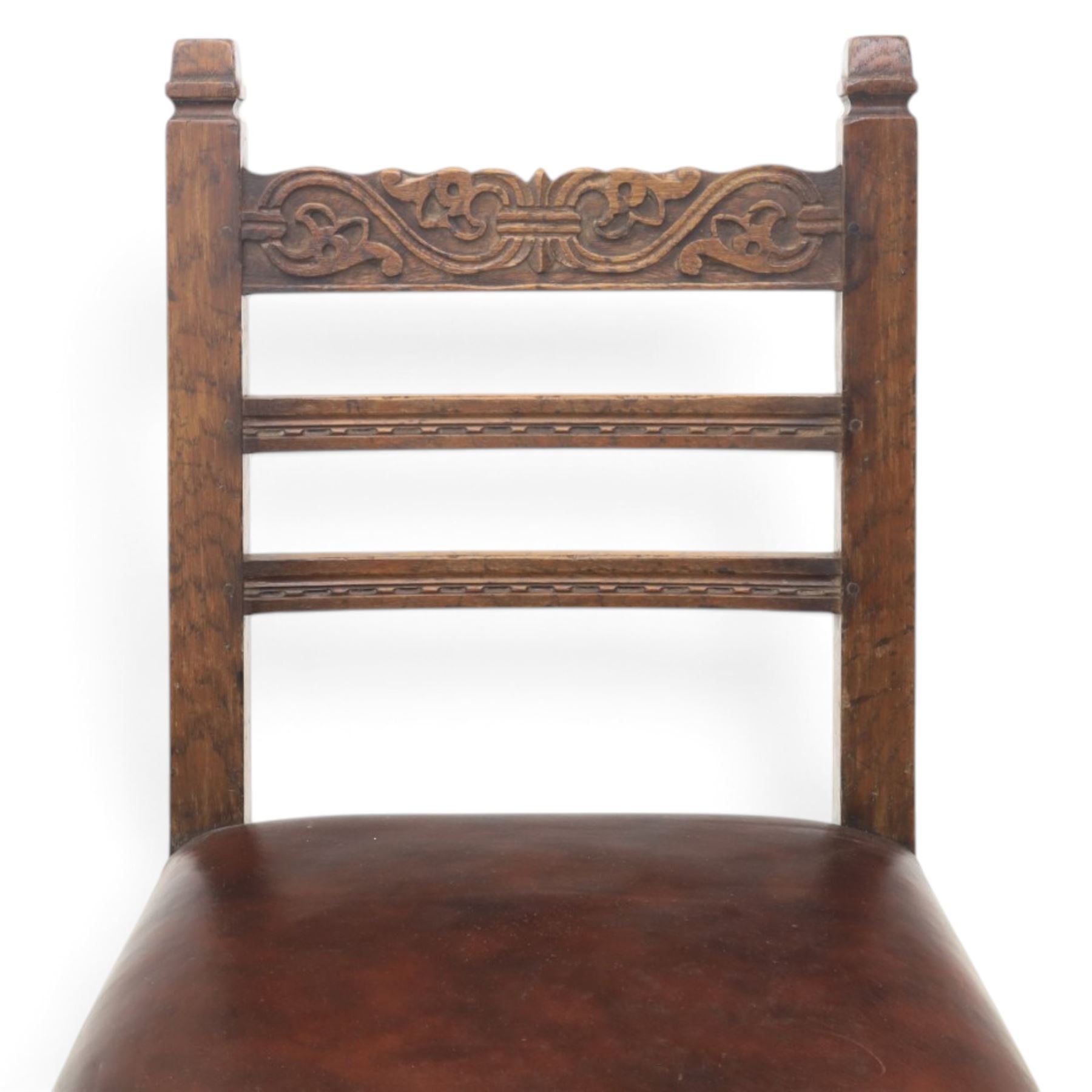 Craftsman made set of four solid oak dining chairs with leather seats, with carved cresting rail, on red leather seats with studded trim, raised on block and turn supports united by H-stretcher