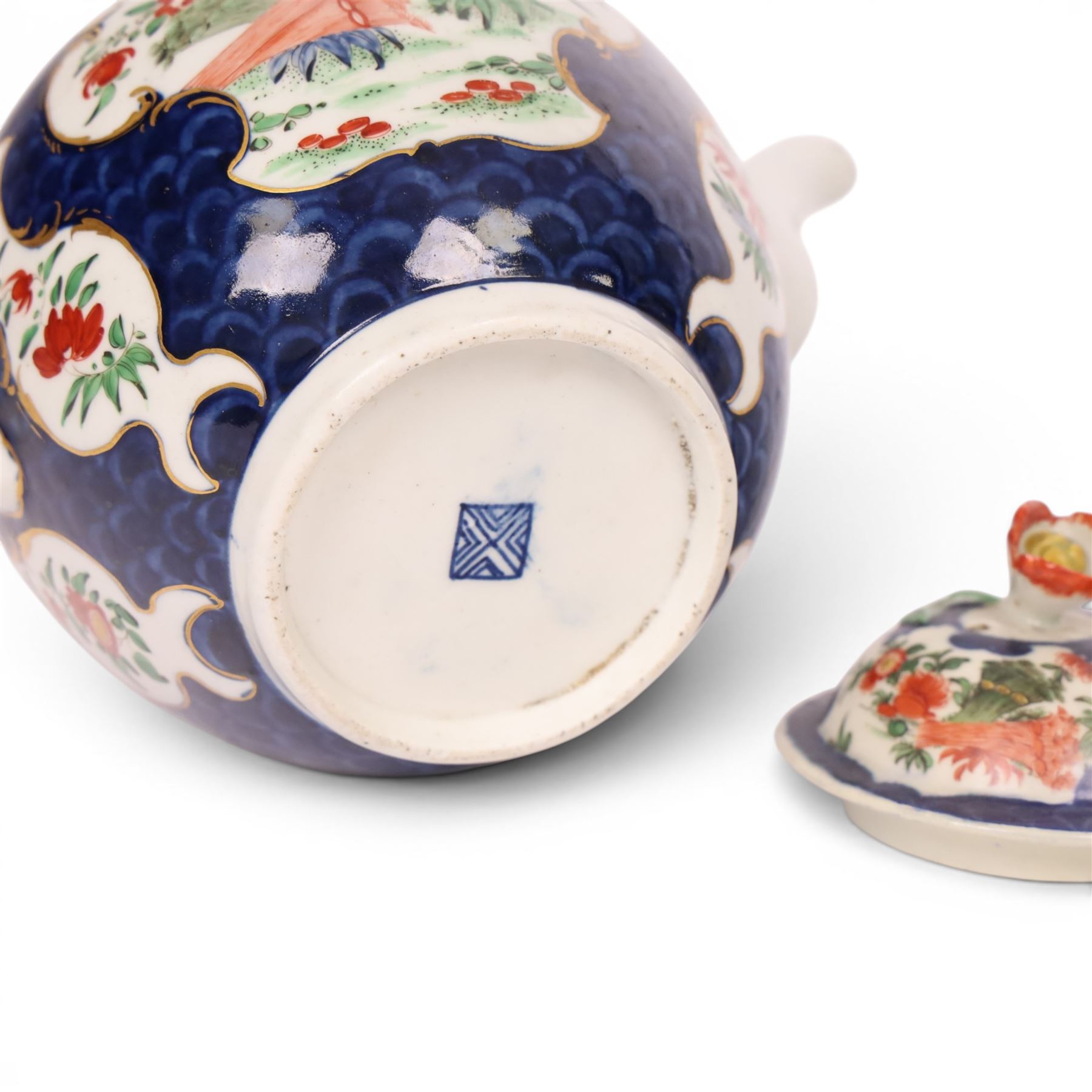18th century Worcester teapot, circa 1763-70, of globular form, painted with shaped panels of chrysanthemums and banded hedges on a blue scale ground, cover with flower finial, mark beneath, H15cm