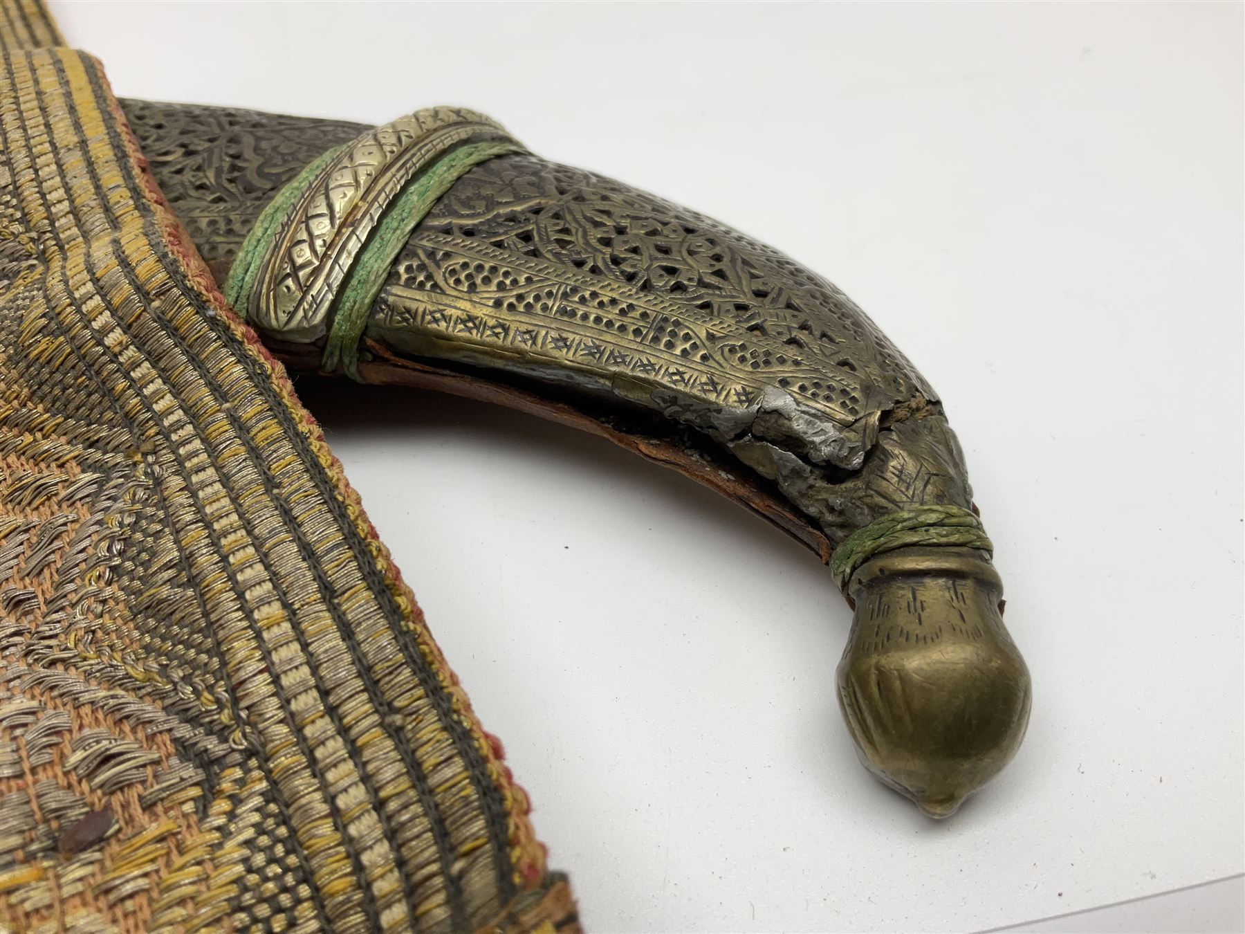 Late 19th century Yemeni Tuza jambiya as worn by religious elite, the 20.5cm curving blade with raised medial ridge, the horn hilt with pique style studwork, in a leather wrapped wooden scabbard with pierced metal mount and leather belt applied with embroidered 'gold' and 'silver' thread work panel; dagger L36cm overall, belt L84cm