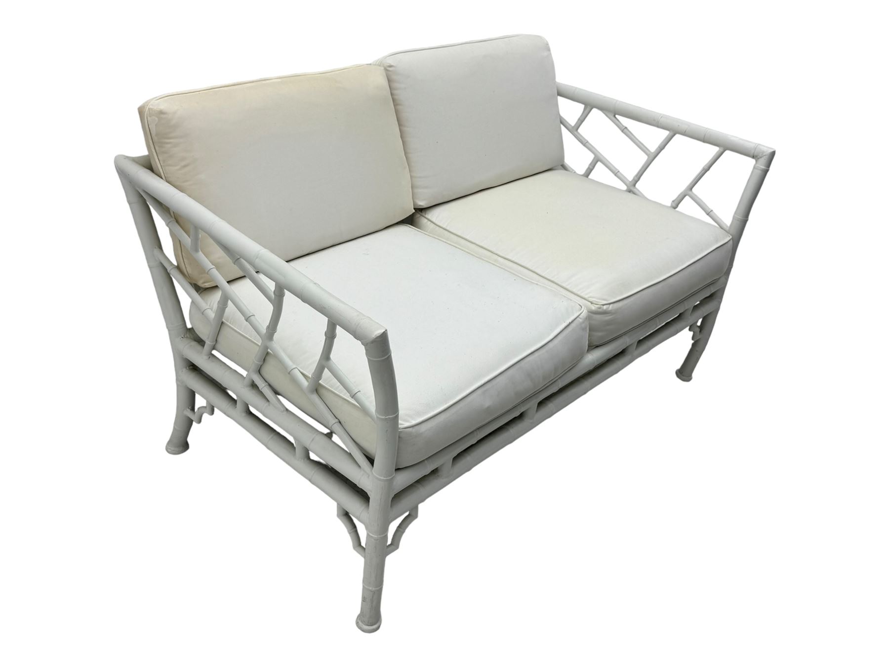 Late 20th century faux bamboo conservatory sofa, white painted frame with geometric openwork back and sides, loose cream cushions, on cylindrical supports (W134cm, D76cm, H80cm); matching armchair (W75cm, D76cm, H80cm); matching coffee table with glass insert (W46cm, D45cm, H36cm)