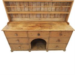 Early 19th century waxed pine farmhouse dresser and rack, the rack featuring two plate shelves and bars above seven drawer base with centre 'dog kennel' recess, raised on turned feet