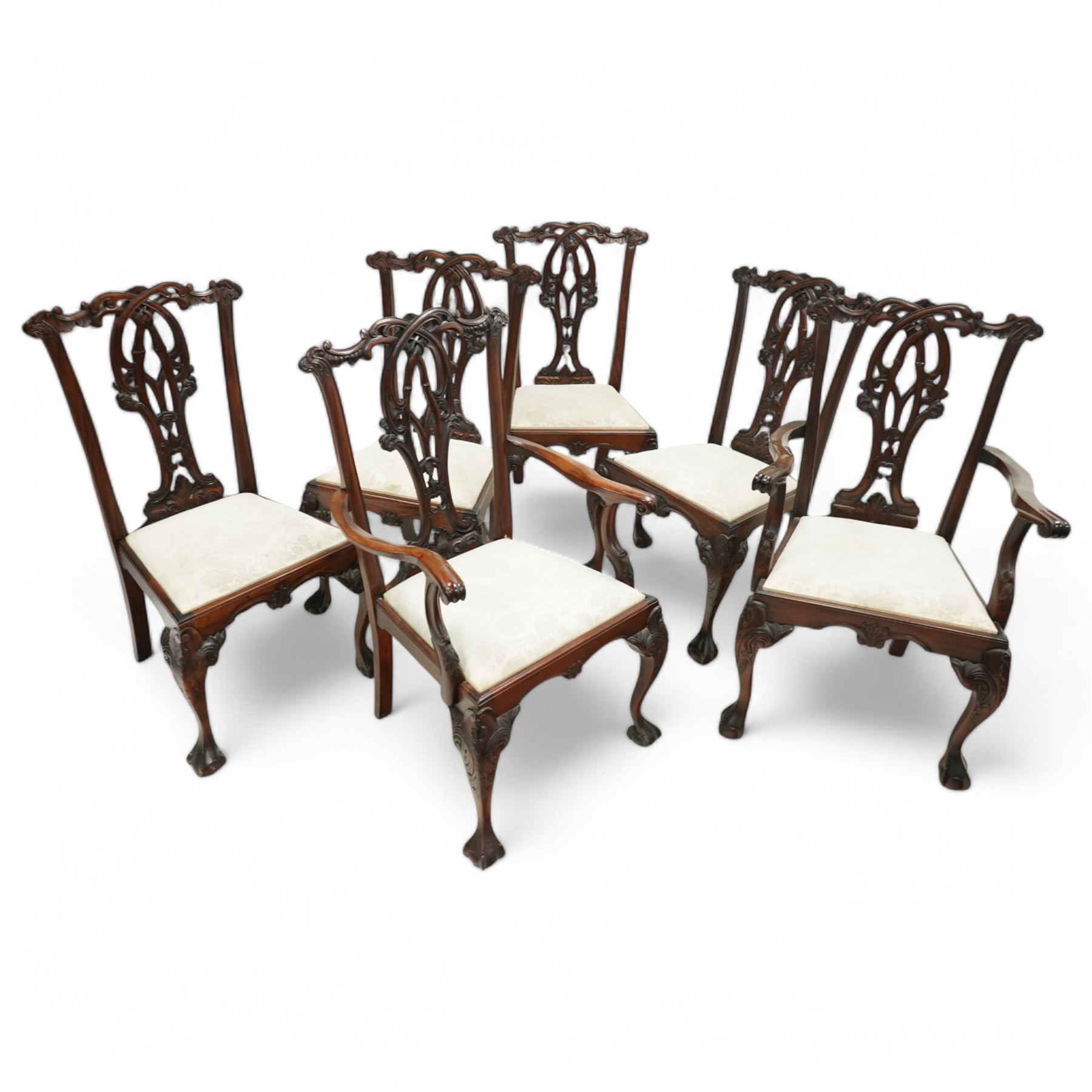 Chippendale revival mahogany dining chairs, set of six including a pair of carvers, the backs with intricately carved pierced splats beneath serpentine cresting rails, on acanthus carved cabriole front supports terminating in claw and ball feet, with cream upholstered drop-in seats