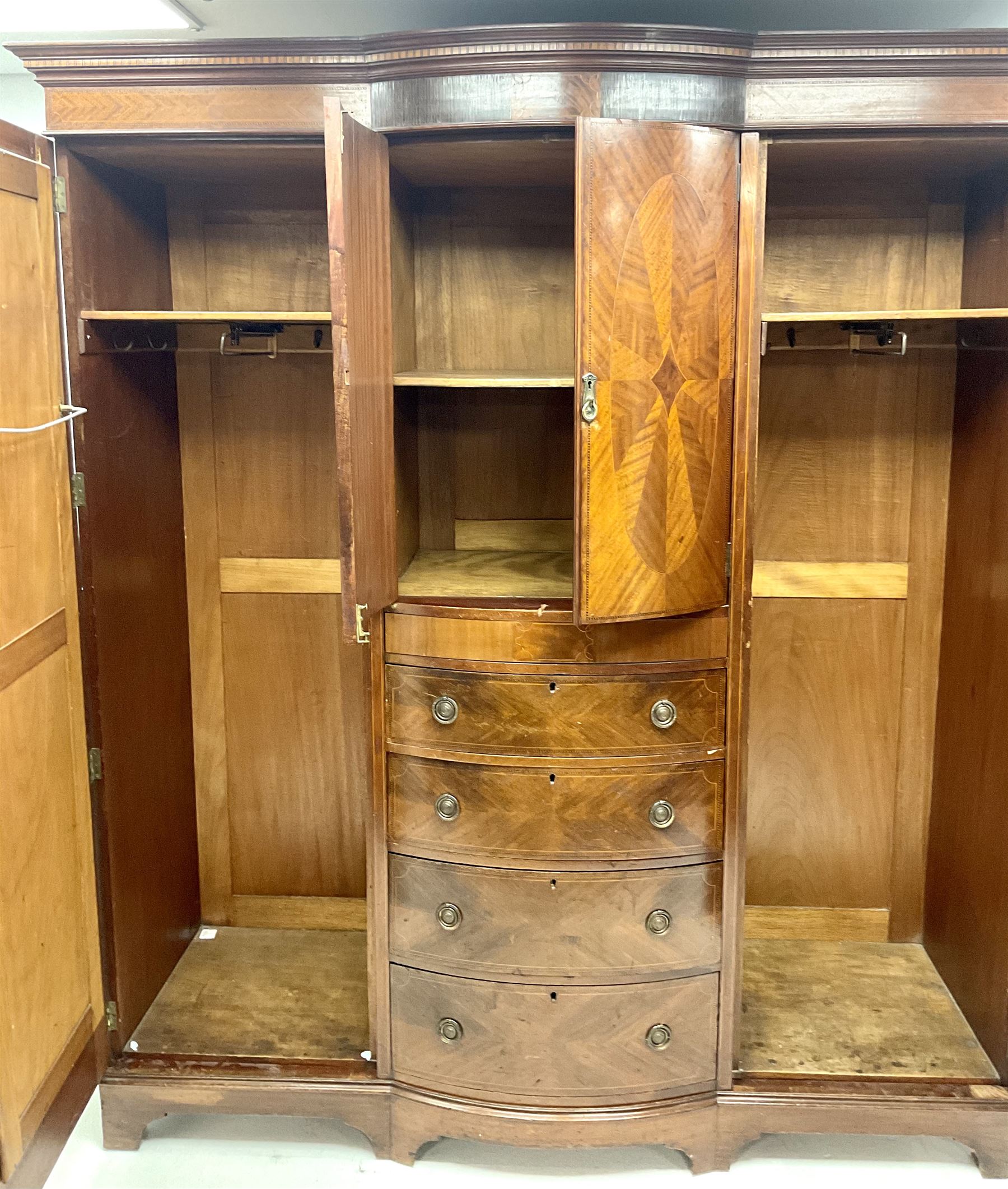 Edwardian inlaid mahogany triple wardrobe, bow front centre with two cupboards above four graduating drawers flanked by two bevel edged mirror doors, shaped platform base 