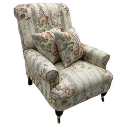 Victorian design armchair, rolled back and arms, upholstered in floral pattern fabric with two scatter cushions, on turned front feet with brass cups and castors