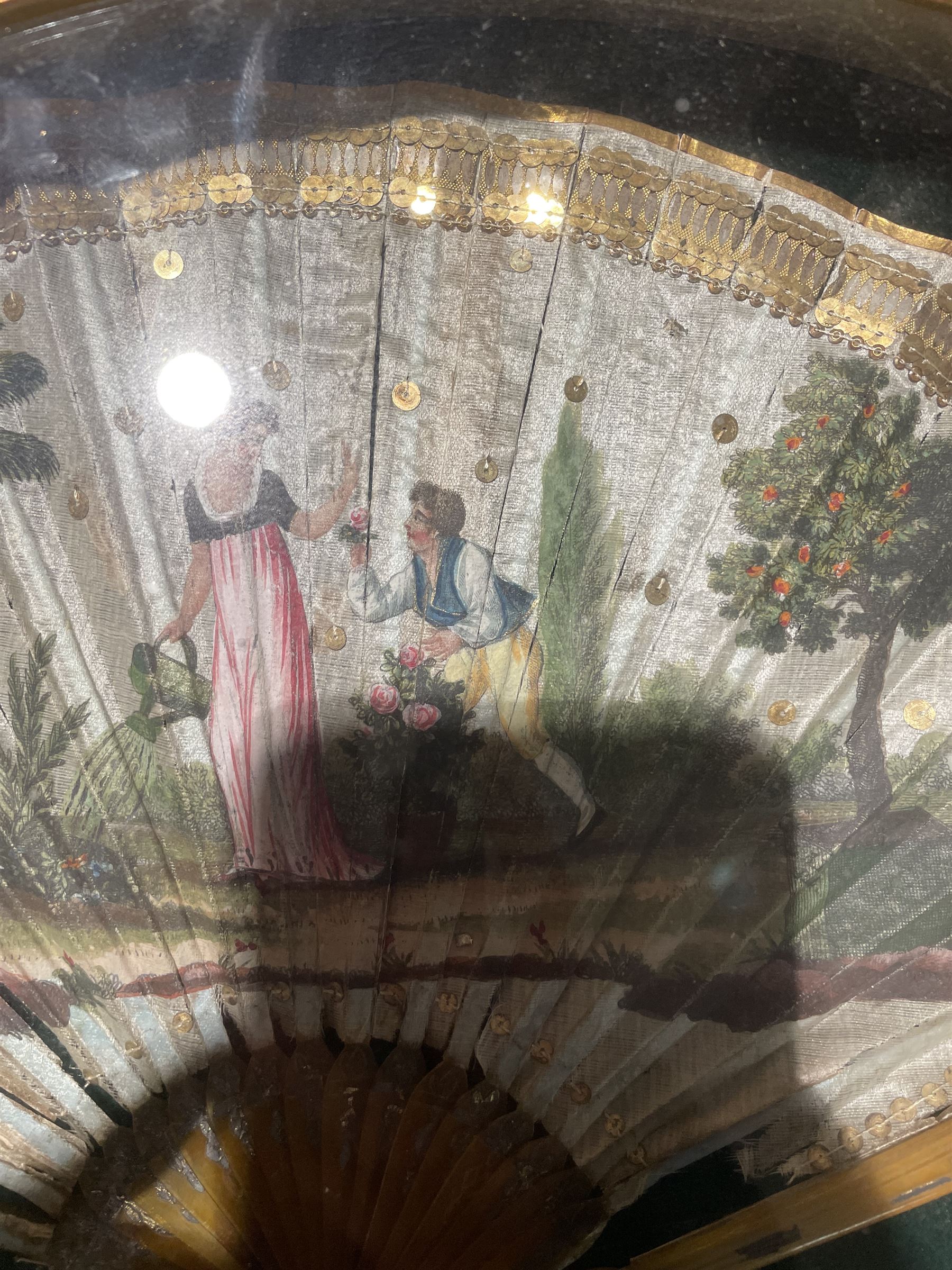 18th century fan, the horn sticks and guard with silvered and gilded decoration, the silk leaf painted in strong colours with a young couple in a garden setting, within a border of gold coloured sequins, framed and glazed, overall H35cm L55cm
Provenance: From the Estate of the late Dowager Lady St Oswald
