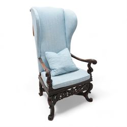 Carolean design walnut and oak wingback open armchair, the high wingback upholstered in light blue herringbone fabric, acanthus leaf carved arms with scrolled terminals and on scrolled supports, cane work seat with squab cushion and scatter cushion, the lower rail carved and pierced with putti holding crown surrounded by curled acanthus leaves, leaf carved S-scroll supports united by Scrolled X-framed stretchers 
