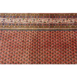 West Persian Boteh-Mir hand-knotted rug, madder red field densely decorated with a repeating lattice of of small boteh motifs arranged in diagonal rows enclosed by a broad border of stylized geometric devices and angular floral ornament between multiple guard stripes with cotton fringe ends