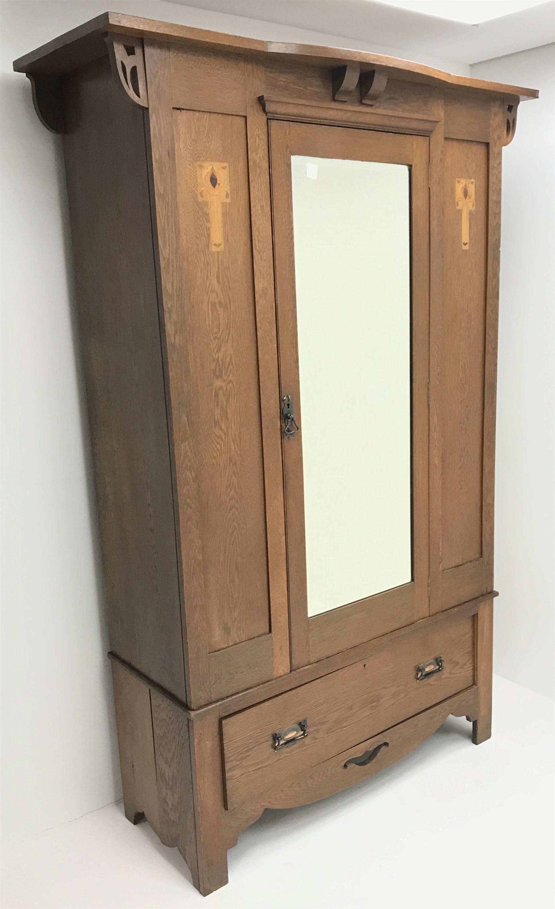 Arts and Crafts period oak wardrobe, projecting shaped cornice, single bevel edged mirrored door above drawer