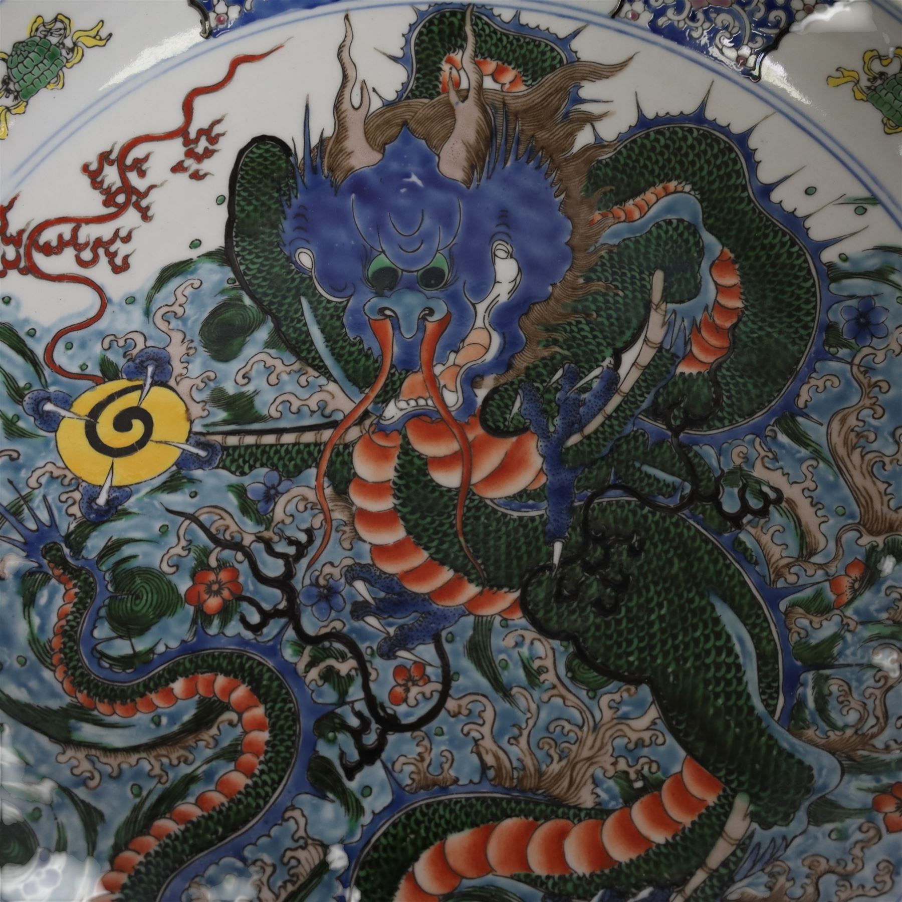 20th century Chinese charger, decorated in blue, green and red enamels with a four clawed dragon chasing the flaming pearl amidst waves and flower heads, the rim with border of alternating reserves of auspicious emblems and flower scrolls, bearing apocryphal Kangxi mark beneath, D38cm 


