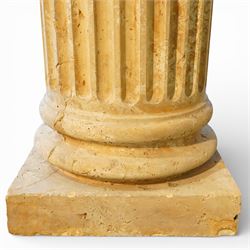 A pair of early 20th century Italian Neoclassical pedestal columns of simplified Doric type; each of fluted cylindrical form in composite stone, finished to evoke weathered limestone or travertine, raised on square plinth bases