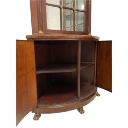 Pair of French Empire design corner cabinets, the straight-front upper section with canted corners and applied half-column pilasters, enclosed by mirror glazed door, the bow-front lower section enclosed by two doors with applied mouldings, mounted by cast metal floral rosettes, skirted base with cast gilt metal hairy paw brass feet