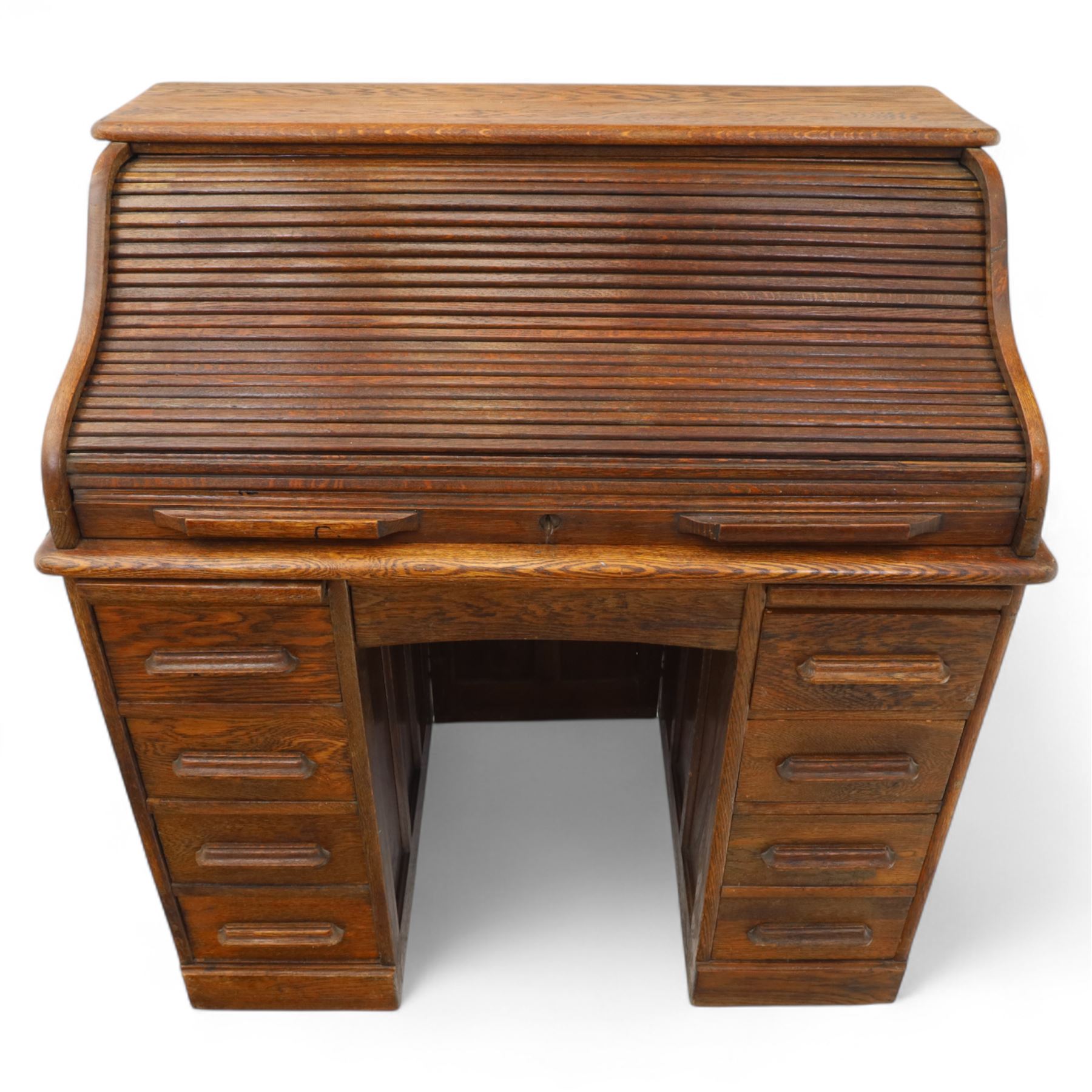 Early 20th-century oak roll-top desk with tambour shutter, enclosing a fitted interior of pigeon holes and small drawers, and pedestal base fitted with nine drawers with moulded handles, raised on plinth base 