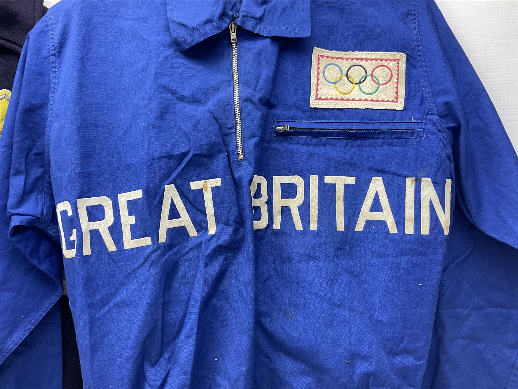 On the direct instructions of Anita Porter nee Lonsbrough Great British Olympic and Commonwealth Games gold medal winning swimmer - collection of early and international memorabilia comprising original Huddersfield Bath Club track suit top bearing eight stitched on cloth badges including British Empire & Commonwealth Games 1958 England Team, YSASA, North Eastern Counties ASA, ESSA Division 3,  English Schools Swimming Association winner etc
The swimming costume Anita wore at the 1958 Commonwealth Games in Cardiff, her first major championships, where she won two gold medals. The grey elastic on the sides, in those days, she would use to make it tighter and more streamlined.
Blue track suit from the 1960 Olympics which she wore on the podium receiving the gold medal.
1960 pool side towelling robe used at the Rome Olympics (interesting to note her name is spelt wrong on the embroidered label).
1962 Commonwealth Games pool side towelling robe used in Perth Australia when winning three Gold medals. 
It was also this year she became BBC Sports Personality of the year, the first female to do so.
Her 'lucky' pool side towel which she took with her to every event she competed in and which can be seen round her neck in many official celebratory photographs. Copies of some of these photographs are included for identification.
In addition there are two souvenir programmes of an evening event to honour Anita at The Theatre Royal Huddersfield and she has kindly signed the front cover on one of these.