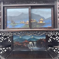 Early 20th century Japanese Meiji style carved hardwood cabinet, of symmetrical tiered form with pierced foliate fretwork panels and phoenix crest, fitted with sliding and hinged doors inset with hand-painted landscape panels depicting Mount Fuji, waterfalls, and lakeside dwellings, raised on shaped bracket supports