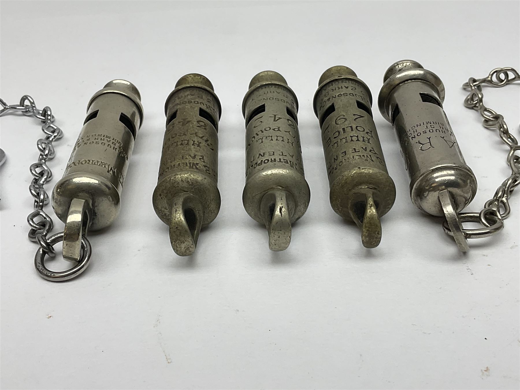 Three Hull City Police 'Metropolitan' whistles by J. Hudson 13 Barr Street Birminham, each with impressed collar number; another 'Metropolitan' police whistle with chain; and an ARP whistle by Hudson & Co with chain (5)