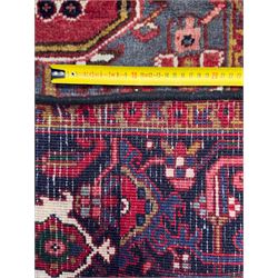 Northwestern Persian Heriz hand-knotted carpet, madder red field with a bold stepped medallion in indigo, ivory, and ivory, surrounded by angular floral motifs and stylized leaves, and the spandrels set within a dark border of rosettes and angular vine motifs, 335cmx252cm