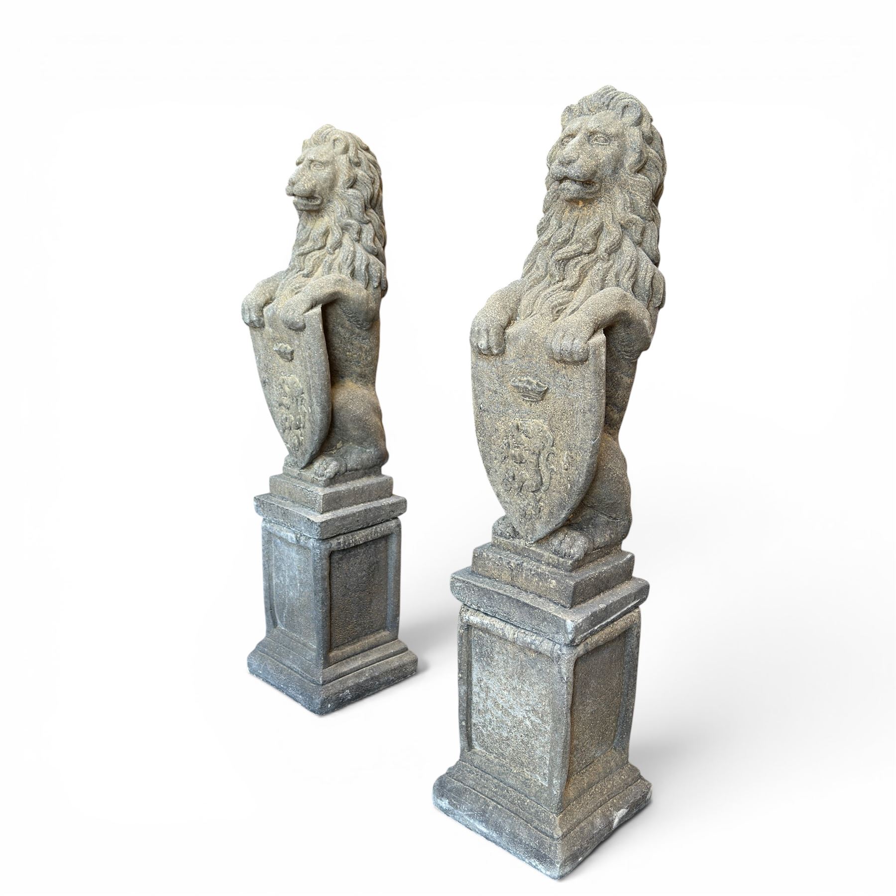 Pair of cast stone Heraldic lions, modelling in upright standing poses with flowing mane, each clasping an Armorial shield moulded with a crowned lion in their forepaws, raised on rectangular pedestals