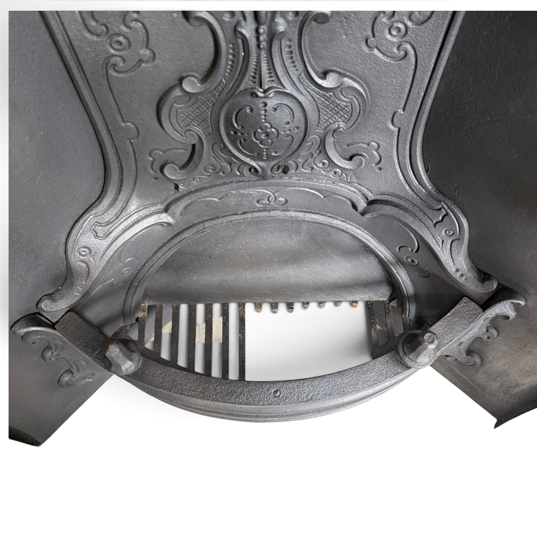 Victorian cast iron fireplace, the arched surround cast with scrolling foliate ornament and central shield-shaped cartouche, fitted with a bowed fire basket, in black painted finish