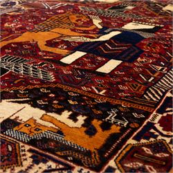 South West Persian Qahqai pictorial hand-knotted rug, madder red field with an all-over pattern of repeating rosettes enclosed with angular leaves and corners with stylized animals figures, central stylized lion in rearing stance and raised forelegs and a human figure shown in profile within a principal border of alternating octagonal and diamond medallions, each enclosing stylized rosettes, flanked by guard stripes incorporating latch hook motifs, with cotton fringe ends  