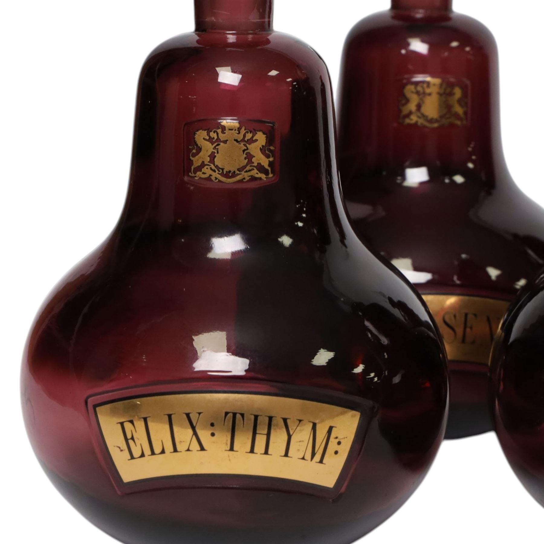 Set of four 20th century Royal Pharmaceutical Society amethyst glass bottles, of bellied form with clear cut glass spire stopper, each body bearing gilt label in Latin: ELIX:THYM:, ELIX:CAMPH:, ELIX:ANIS: and ELIX:SENN:, and gilt Royal Pharmaceutical Society crest to neck, H25cm

Provenance: From the collection of the family of Peter Green, a practising pharmacist whose career spanned the mid to late 20th century. During his professional life he managed pharmacies in Yeovil, Somerset, and later Selles Chemist in Filey, North Yorkshire, before purchasing and running his own business, Peter Green Pharmacy, located in the Market Place, Malton. The bottles were displayed as part of the traditional shop fittings in both the Filey and Malton pharmacies and were retained as part of his collection.