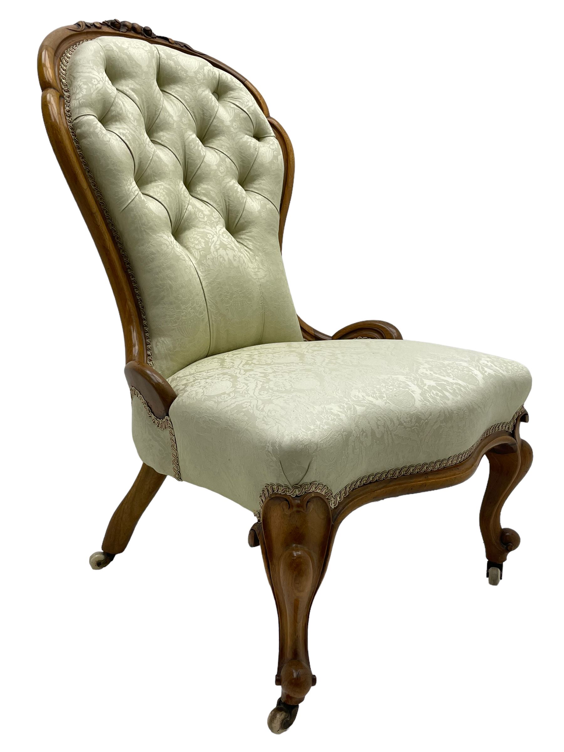 Victorian walnut framed nursing chair, the cresting rail decorated with carved applied flower heads and acanthus leaves, shaped back and sprung seat upholstered in buttoned ivory damask fabric, serpentine front over cartouche carved cabriole supports with ceramic castors (W57cm H92cm); with matched footstool, circular top over shaped moulded apron, on floral carved cabriole feet (W34cm) 