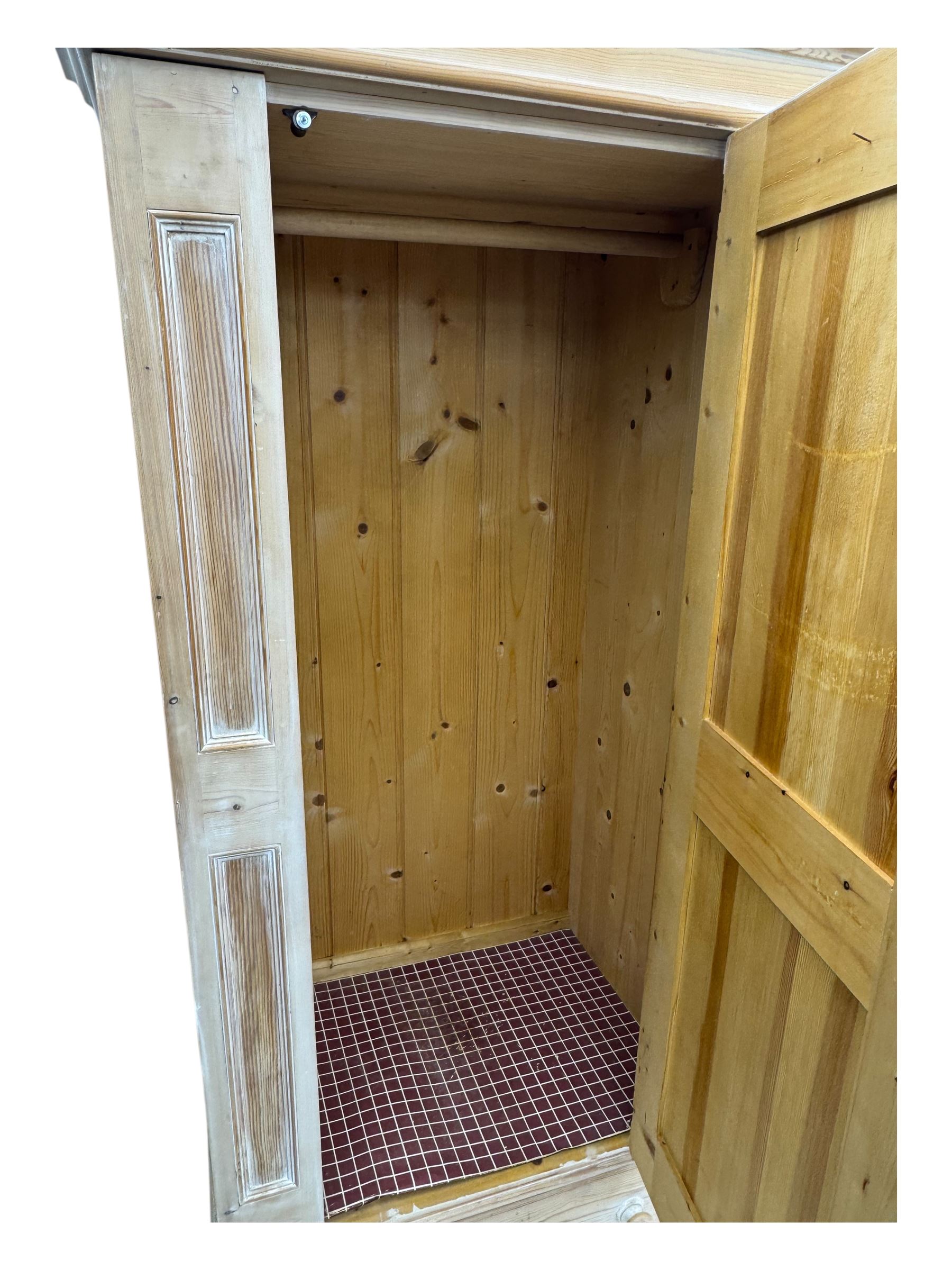 Victorian design lime-washed pine single wardrobe, projecting cornice over panelled door enclosing hanging rail, the lower section fitted with full-width drawer, on shaped plinth base