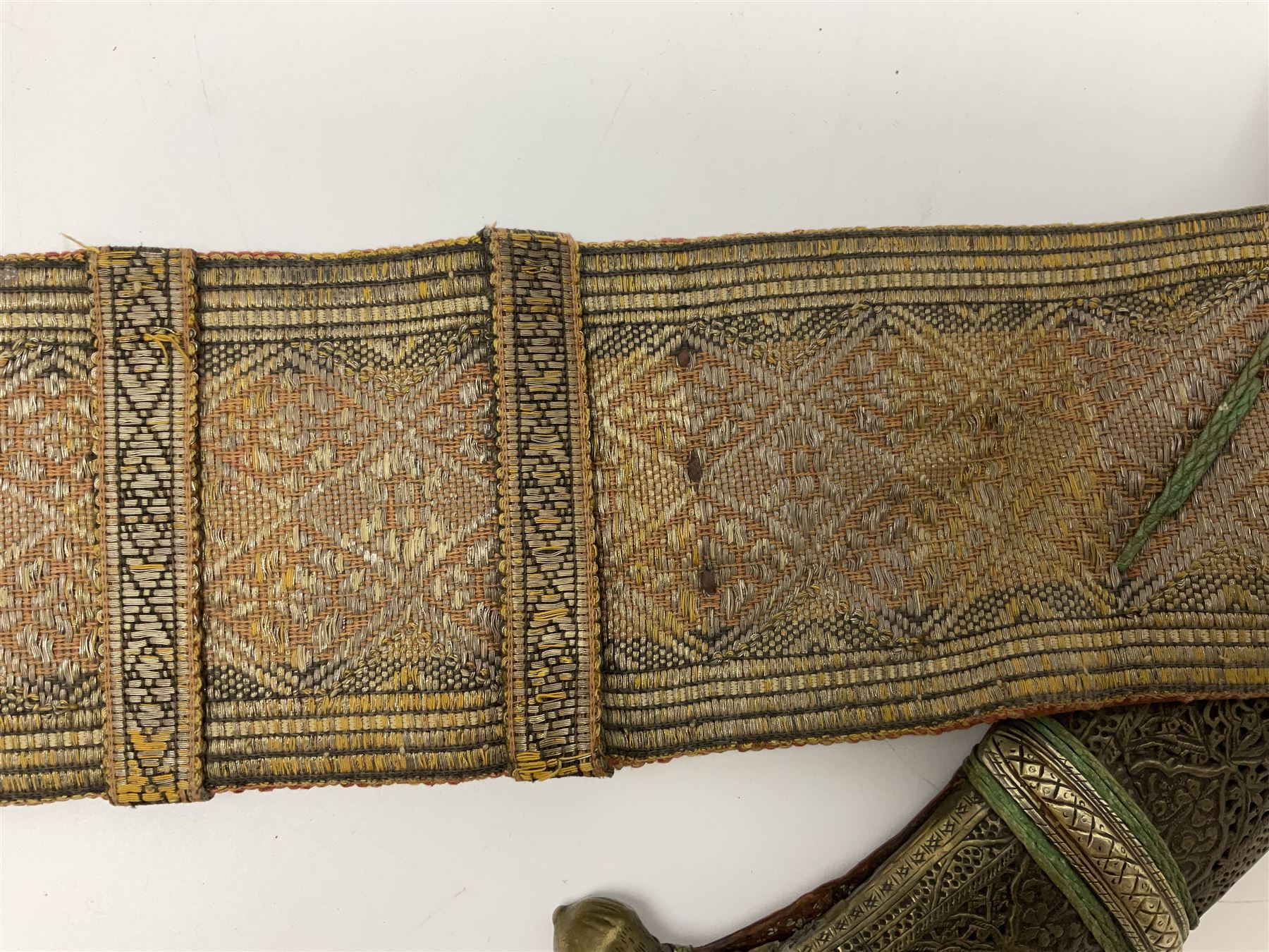 Late 19th century Yemeni Tuza jambiya as worn by religious elite, the 20.5cm curving blade with raised medial ridge, the horn hilt with pique style studwork, in a leather wrapped wooden scabbard with pierced metal mount and leather belt applied with embroidered 'gold' and 'silver' thread work panel; dagger L36cm overall, belt L84cm