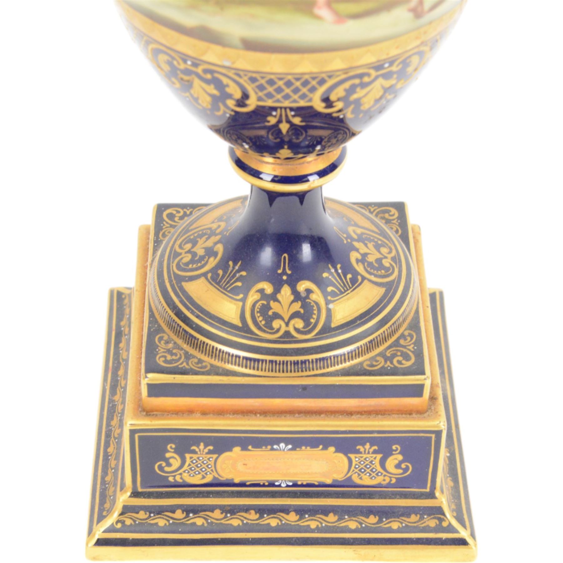 Late 19th century Vienna twin handled urn and cover decorated with classical figures on a textured gilt ground,  upon a square stepped cobalt blue pedestal with gilt detailing, H36cm