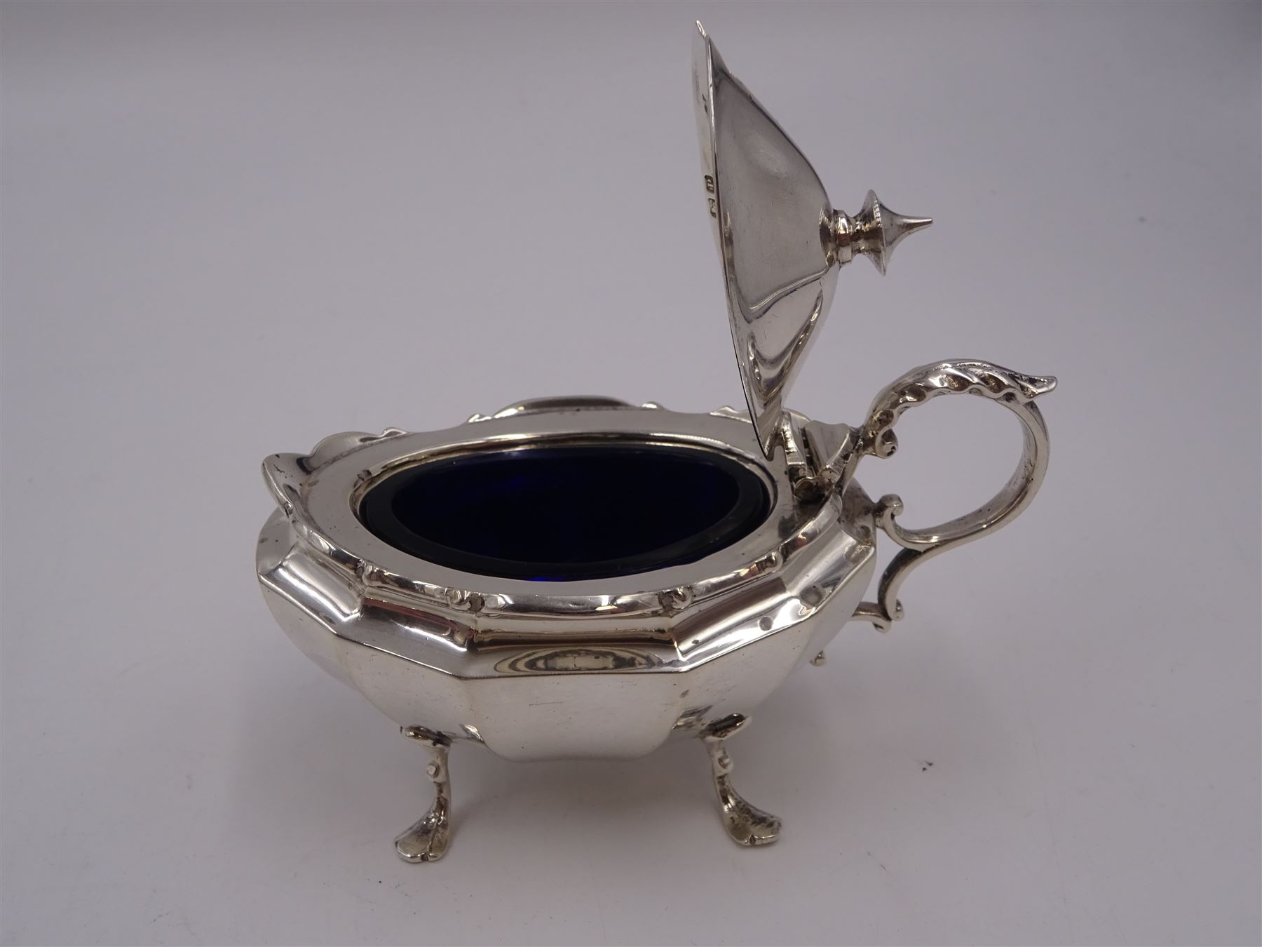 Early 20th century silver mustard pot and cover, of faceted oval form, with shaped rim and acanthus capped scroll handle, upon four pad feet, with matching spoon, H5.5cm, hallmarked I S Greenberg & Co, Birmingham 1912 & 1914, with blue glass liner, together with pair of Victorian silver open salts, of fluted circular form, with lobed rim, upon three pad feet, with matching salt spoons, all hallmarked Atkin Brothers, Sheffield 1899 and a Victorian silver pepper, of waisted baluster form, the part fluted body repousse decorated with flowers and leaves and a floral garland to upper rim, hallmarked William Oliver, Birmingham 1900