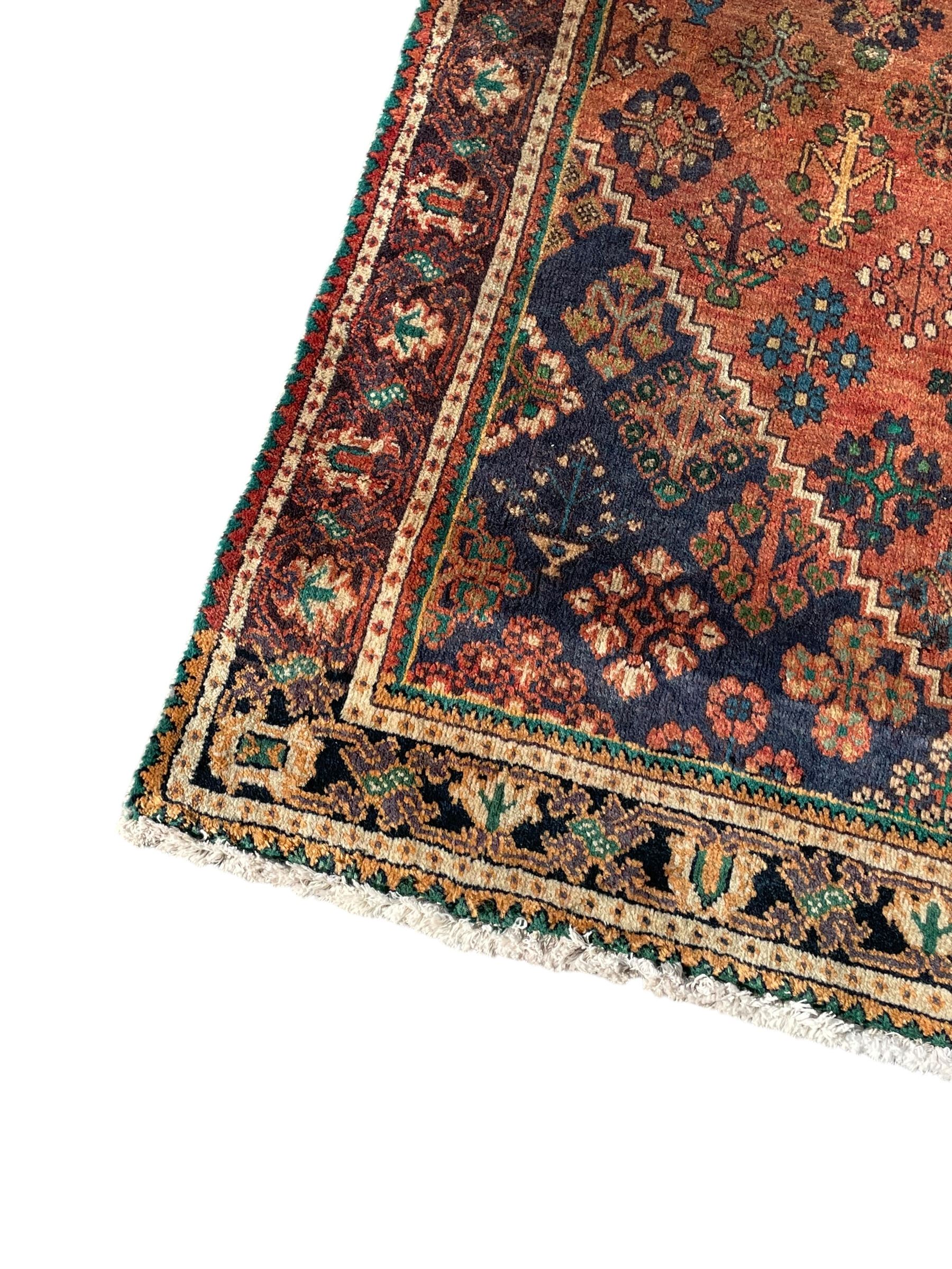 Persian Joshaghan rust ground rug, stepped lozenge medallion surrounded by repeating foliate lozenge motifs, the border decorated with stylised plant motifs, within geometric guard stripes
