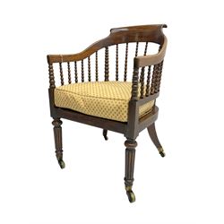 William IV rosewood tub armchair, the arched bow cresting rail over graduated bobbin turned spindles, cane seat with loose cushion, terminating in brass cups and castors.