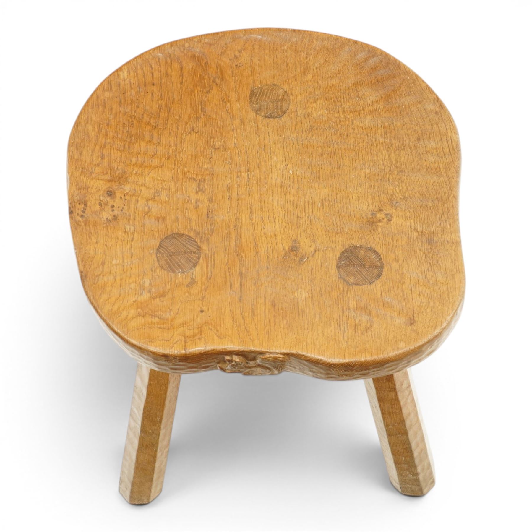 Squirrelman - rustic oak milking stool, adzed shaped top with exposed peg construction, on three tapering supports, with large carved squirrel signature, by Wilf Hutchinson, Husthwaite
