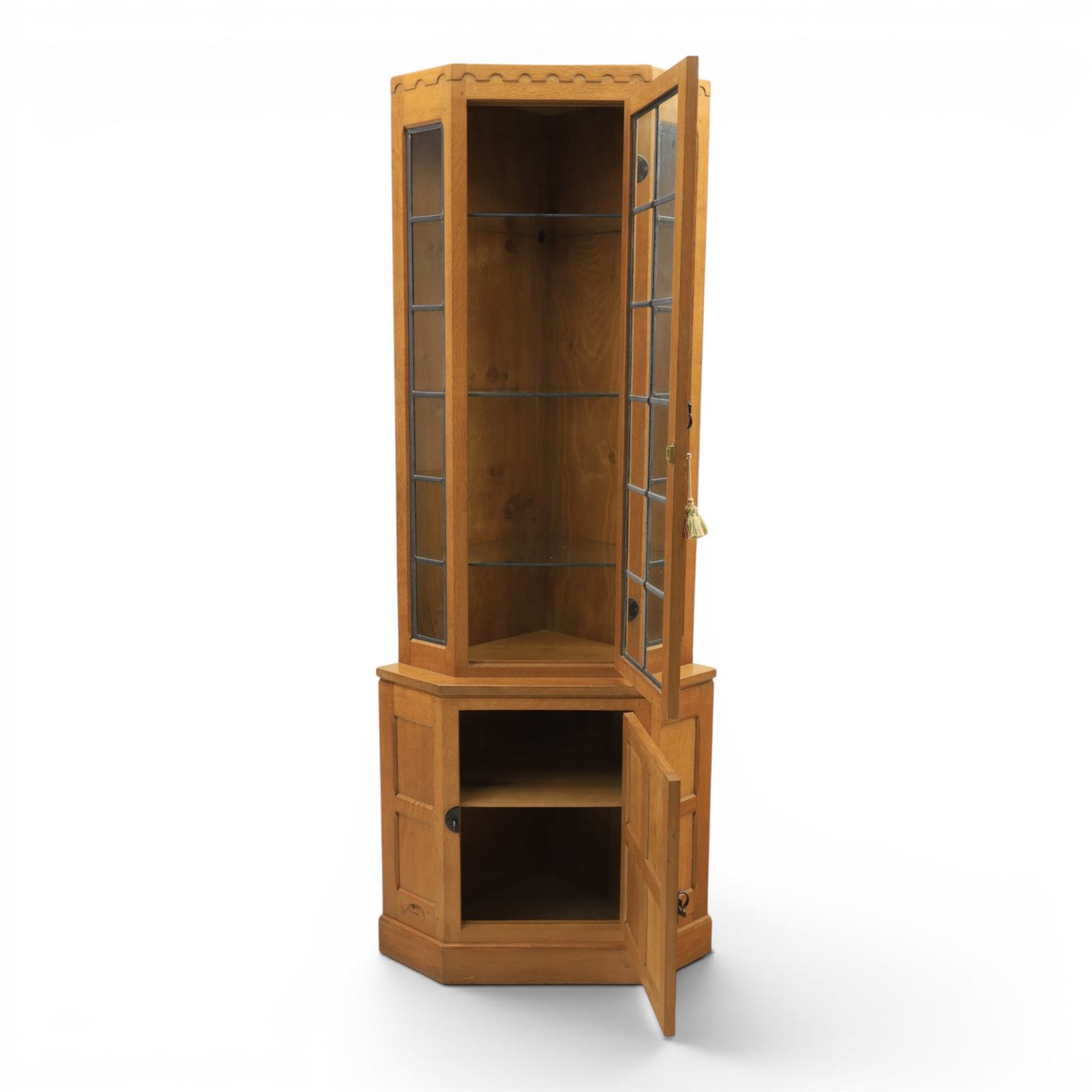 Mouseman - oak floor standing corner cabinet, scalloped cornice above a leaded glass cabinet, blackened metal hinges and latches, with carved mouse by the workshop of Robert Thompson of Kilburn