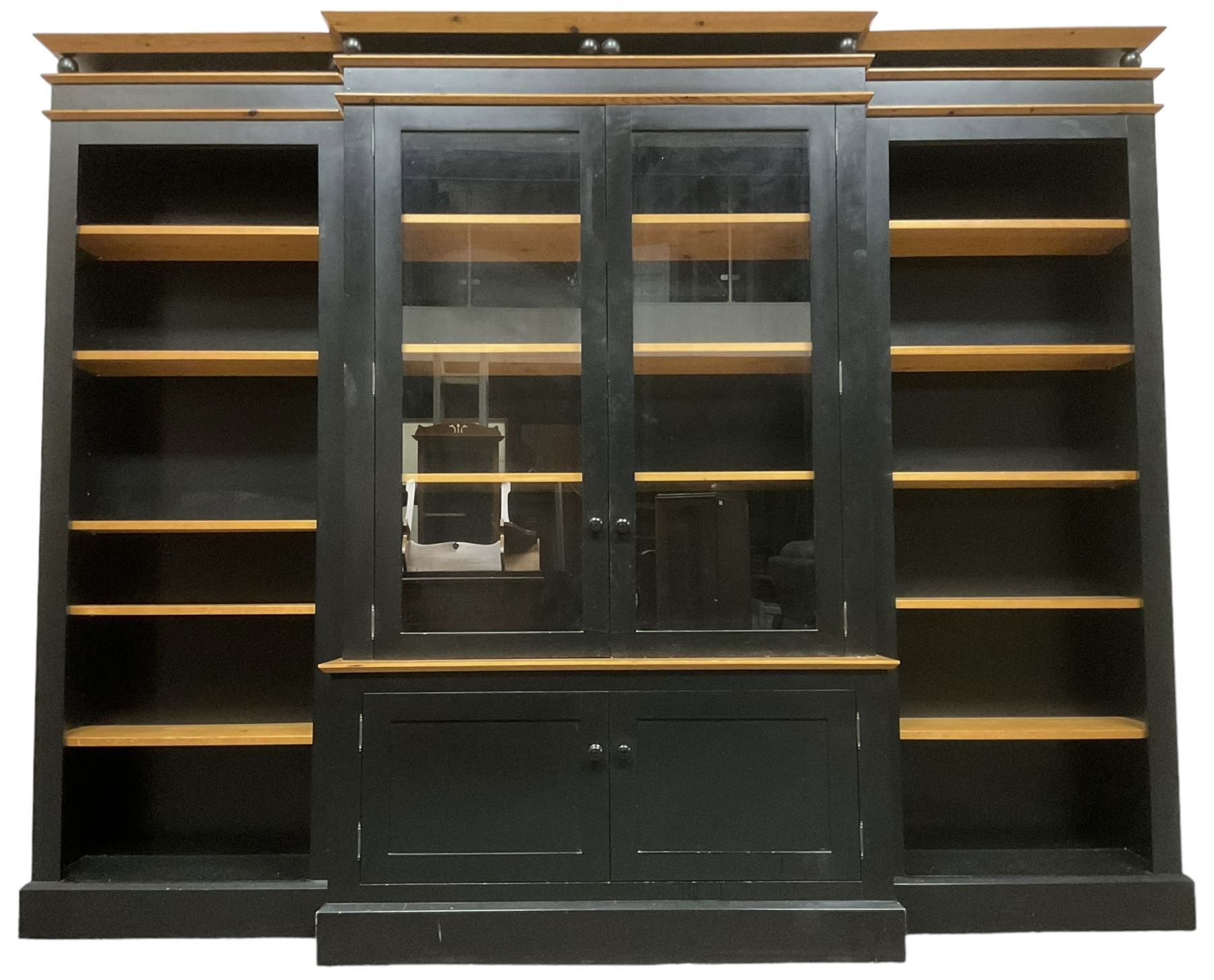 Contemporary polished pine and black finish break-front bookcase, projecting cornice over globular mounts, central cabinet enclosed by two glazed doors over double panelled cupboard, flanked by adjustable shelves, on plinth base