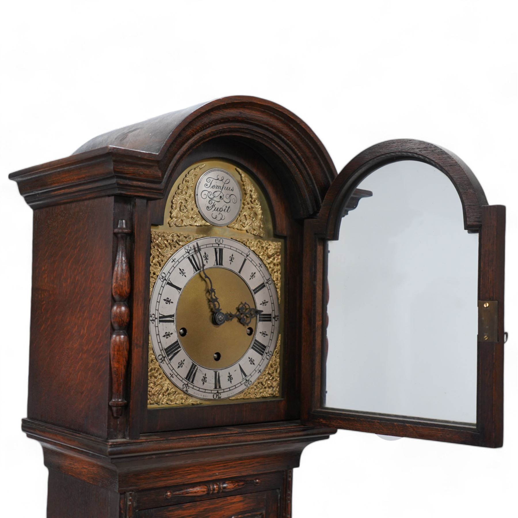 Oak cased 8-day grandmother clock c 1930 - with a broken arched pediment and break arch hood door flanked by turned pilasters, carved full length trunk door on a short plinth raised on bun feet, brass dial with cast spandrels, matted dial centre and silvered chapter with Roman numerals, three train spring driven movement chiming the quarters and hours on 8 gong rods.  With pendulum.