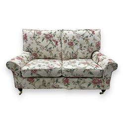 Steed Upholstery - 'Knightsbridge' two seater sofa, upholstered in cream fabric with pink and green floral design, loose back and seat cushions, raised on mahogany supports with brass castors