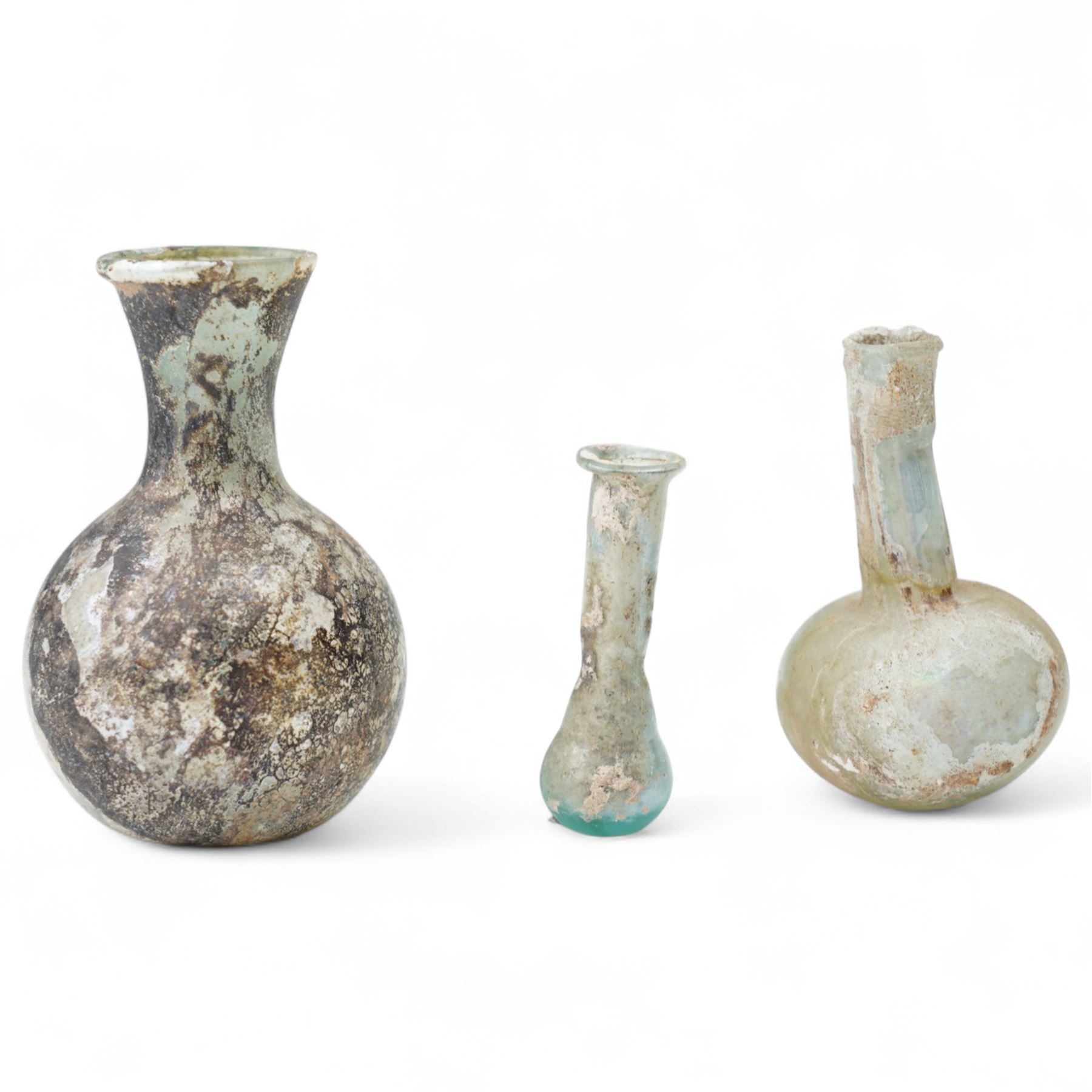Three Roman glass funerary vessels c. 1st-3rd century AD, comprising a group of free-blown glass vessels: two unguentaria with elongated necks and rounded bases, and one squat lachrymatory or tear bottle, heights: 7.5cm, 6.5cm and 5cm
Notes: Unguentaria held oils/perfumes; small bottles of this type are traditionally described as ‘lachrymatories’, though their practical use is generally associated with unguents
Provenance: By the vendor’s repute, acquired/collected in the Middle East (Dead Sea area/Syria) in the 1960s